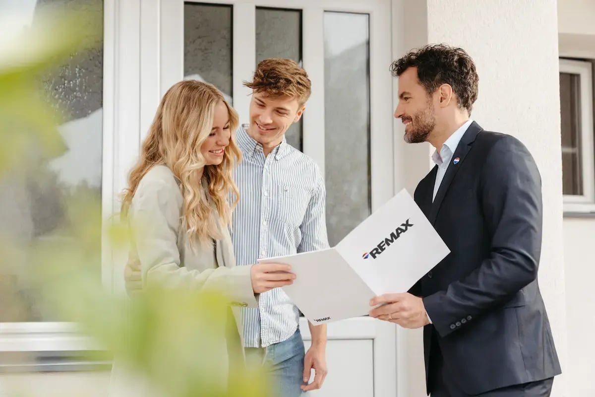 una giovane coppia di clienti con un agente remax che mostra i documenti della casa da visitare
