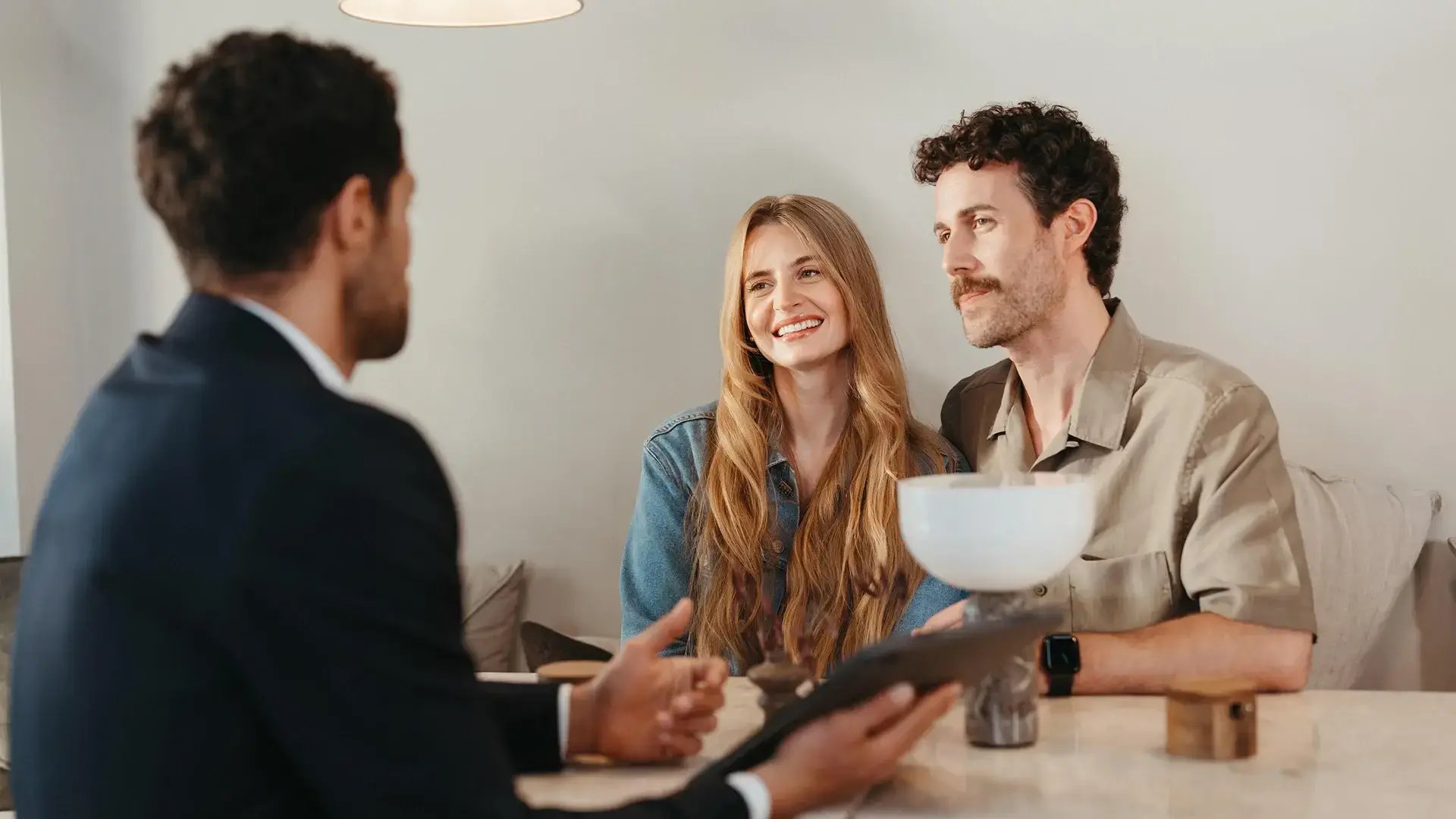 Agente immobiliare mostra una casa su tablet a una coppia sorridente durante una visita, in un ambiente luminoso e moderno.
