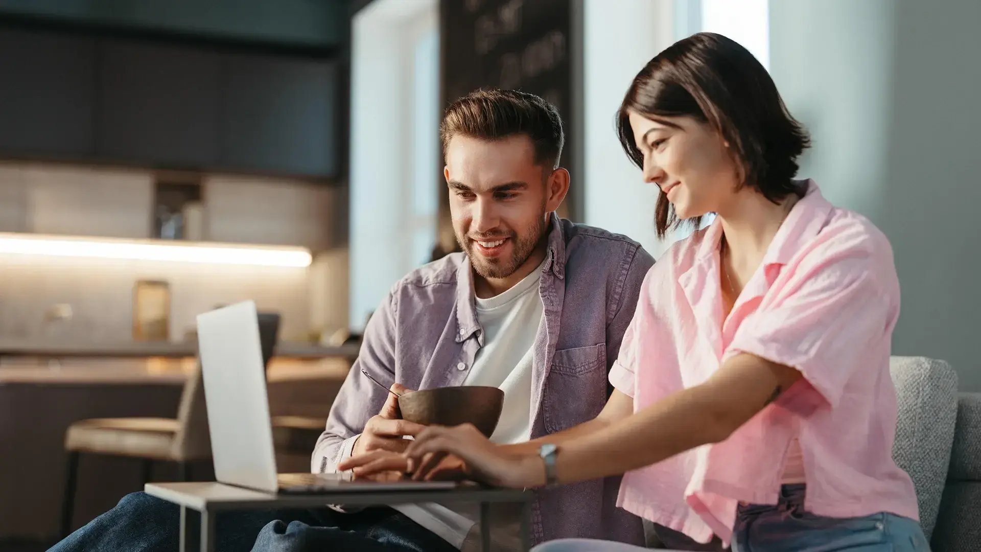 Coppia sorridente davanti a un computer mentre cerca online una nuova casa e consulta proposte immobiliari